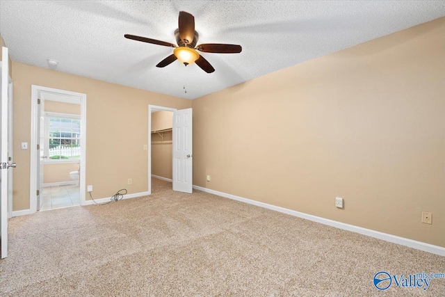 unfurnished bedroom featuring a closet, a walk in closet, a textured ceiling, ceiling fan, and light colored carpet