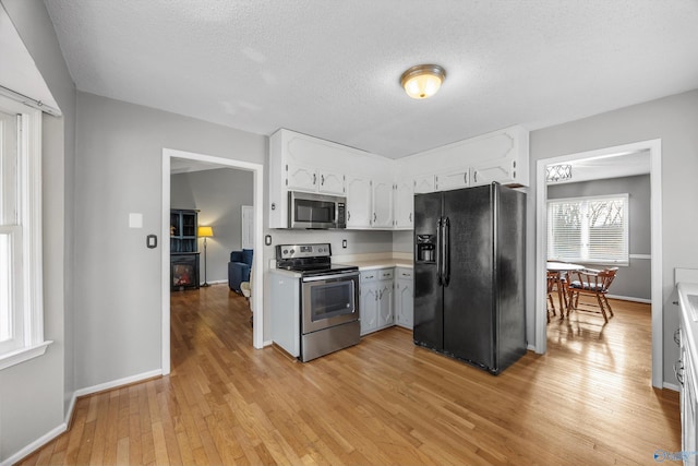 kitchen with a textured ceiling, stainless steel appliances, light hardwood / wood-style floors, and white cabinets