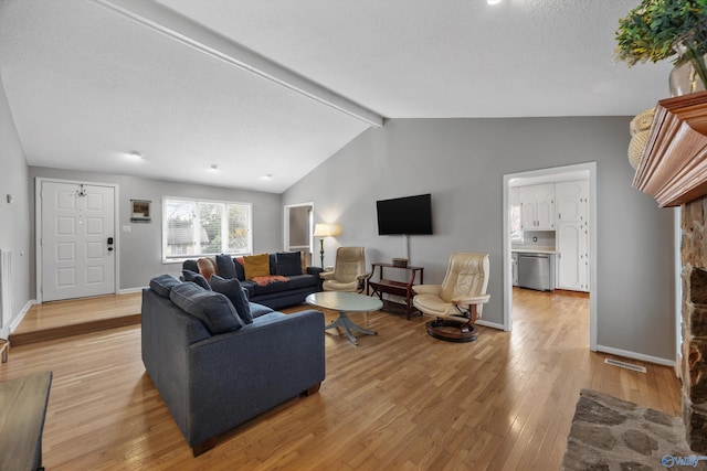 living room with lofted ceiling with beams, a textured ceiling, and light wood-type flooring