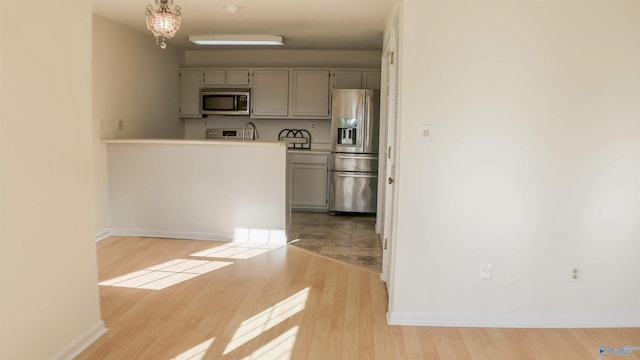 kitchen with appliances with stainless steel finishes, gray cabinetry, hanging light fixtures, a notable chandelier, and light hardwood / wood-style floors