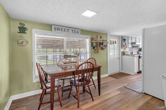 dining area featuring baseboards, light wood-style floors, and a textured ceiling