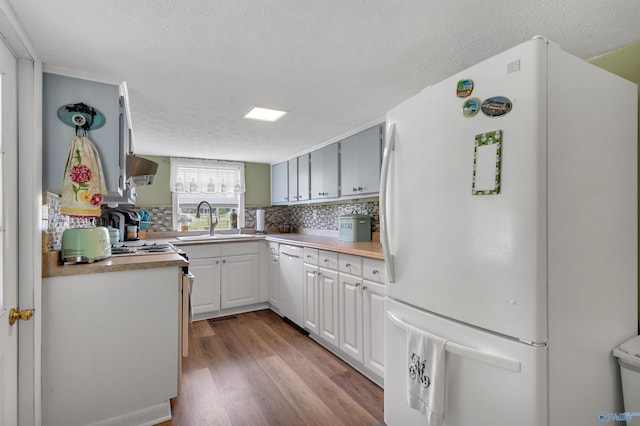 kitchen with light wood-style flooring, decorative backsplash, a sink, and white appliances