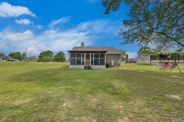 back of house featuring a yard, a sunroom, a chimney, and metal roof