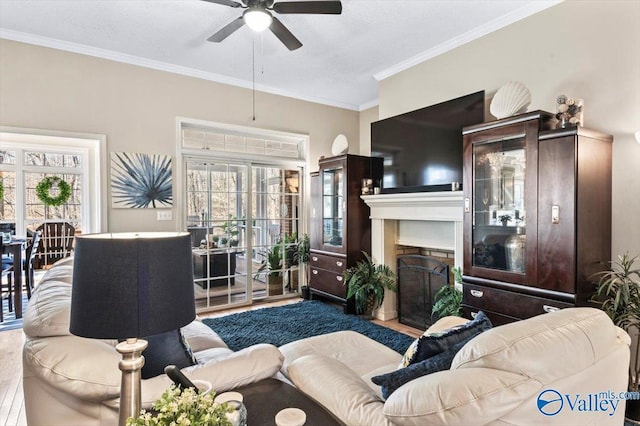 living room featuring a brick fireplace, crown molding, a ceiling fan, and wood finished floors