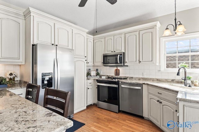 kitchen with light stone counters, light wood finished floors, a sink, hanging light fixtures, and appliances with stainless steel finishes