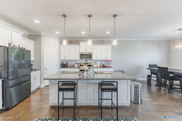 kitchen featuring white cabinets, hanging light fixtures, an island with sink, and stainless steel appliances