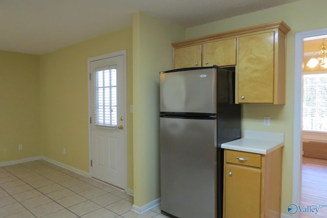 kitchen with a notable chandelier, plenty of natural light, stainless steel refrigerator, and light tile patterned floors