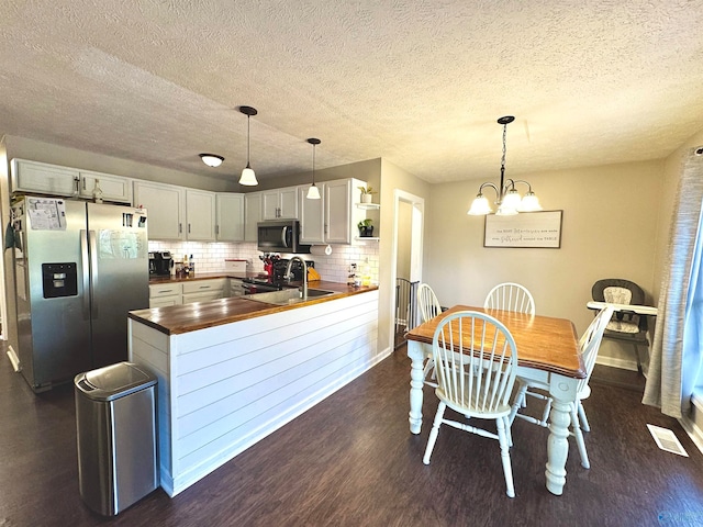 kitchen with dark wood-type flooring, backsplash, a textured ceiling, decorative light fixtures, and appliances with stainless steel finishes