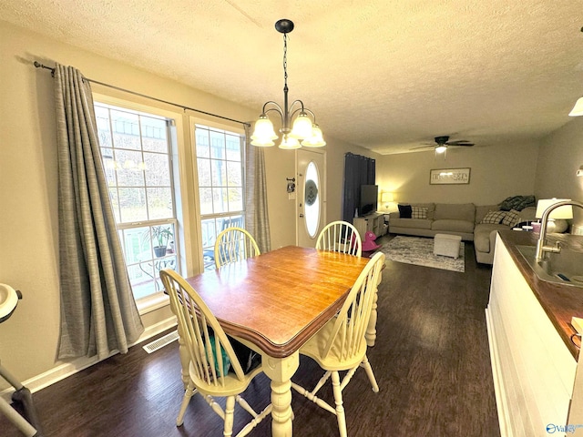 dining area featuring a textured ceiling, ceiling fan with notable chandelier, and dark wood-type flooring