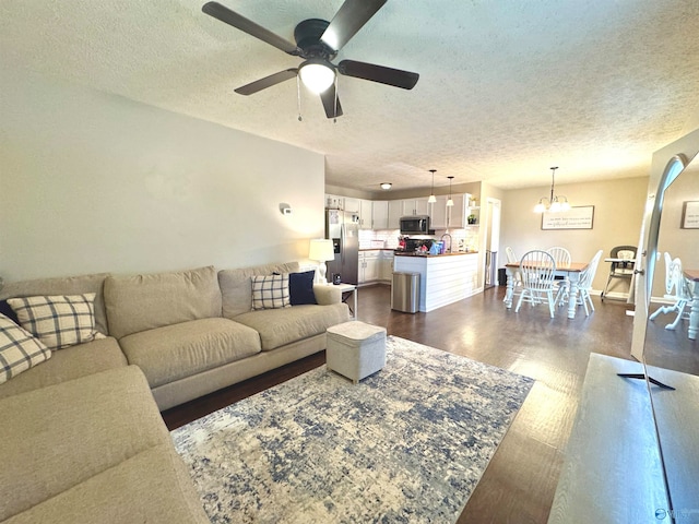 living room featuring sink, ceiling fan with notable chandelier, dark hardwood / wood-style floors, and a textured ceiling