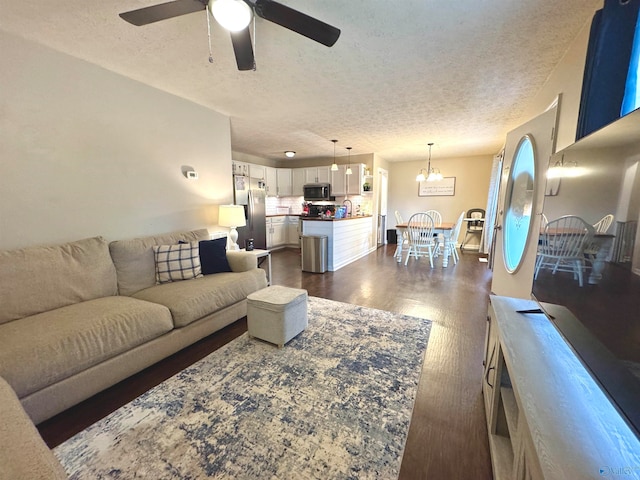 living room with a textured ceiling, dark hardwood / wood-style flooring, ceiling fan with notable chandelier, and sink