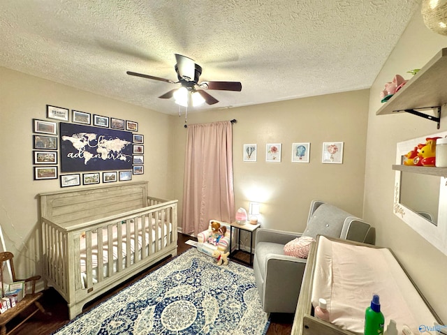 bedroom featuring ceiling fan, wood-type flooring, a crib, and a textured ceiling