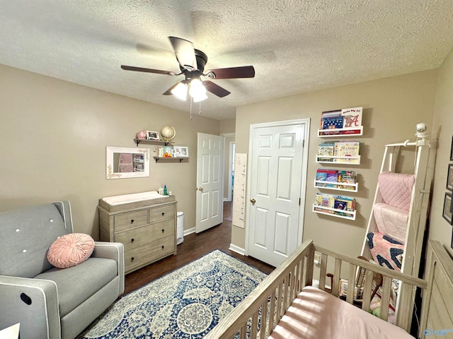 bedroom featuring a textured ceiling, ceiling fan, dark wood-type flooring, and a crib