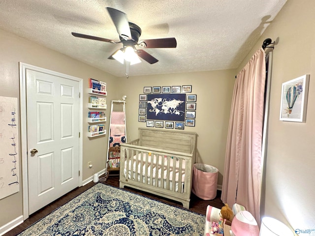 bedroom featuring a textured ceiling, a nursery area, dark wood-type flooring, and ceiling fan