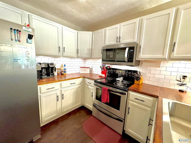 kitchen with appliances with stainless steel finishes, tasteful backsplash, a textured ceiling, dark wood-type flooring, and butcher block countertops