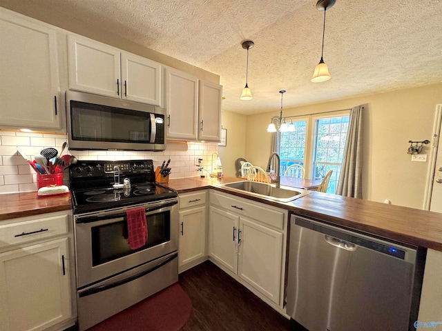 kitchen featuring wooden counters, appliances with stainless steel finishes, sink, decorative light fixtures, and white cabinetry