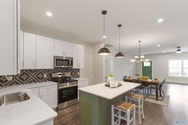 kitchen with a kitchen island, pendant lighting, white cabinets, a kitchen breakfast bar, and stainless steel appliances