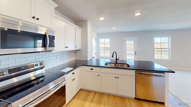 kitchen featuring tasteful backsplash, appliances with stainless steel finishes, white cabinetry, light hardwood / wood-style floors, and sink