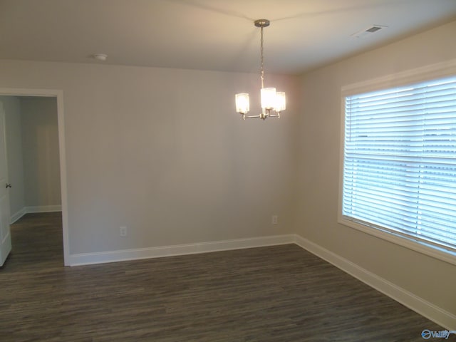 spare room with an inviting chandelier, a healthy amount of sunlight, visible vents, and dark wood-style flooring