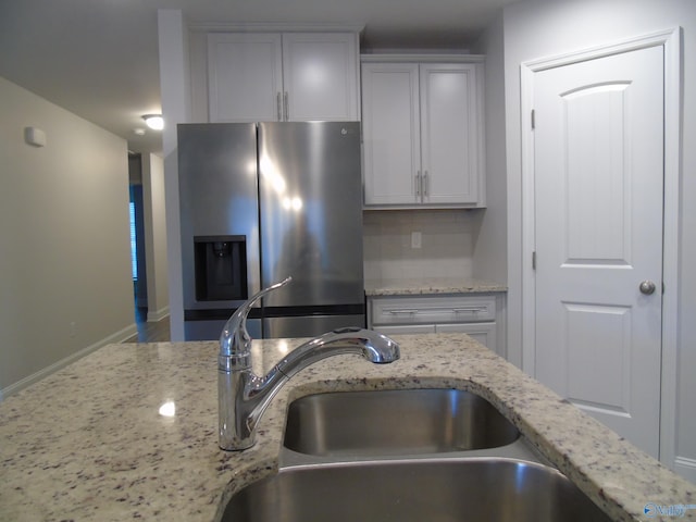 kitchen with light stone counters, stainless steel fridge with ice dispenser, backsplash, and a sink