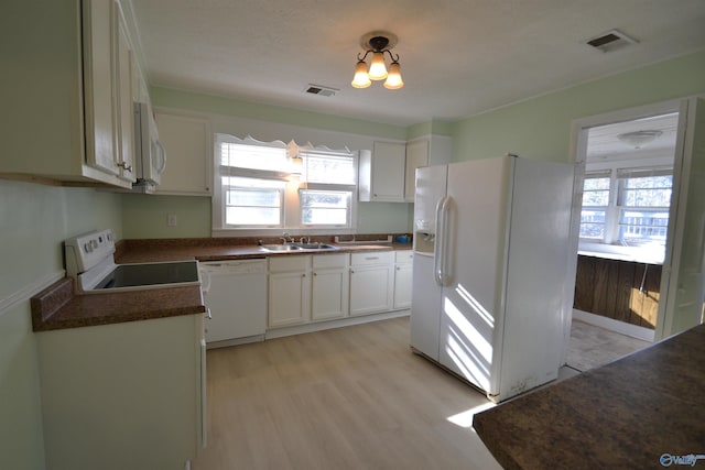 kitchen with visible vents, a sink, dark countertops, white appliances, and white cabinets