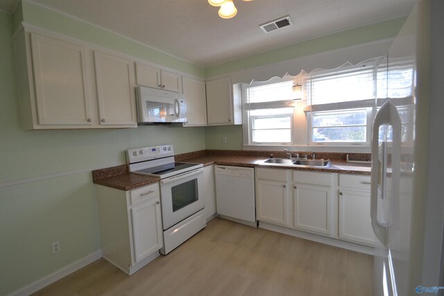 kitchen featuring white appliances, visible vents, a sink, light wood-style floors, and dark countertops