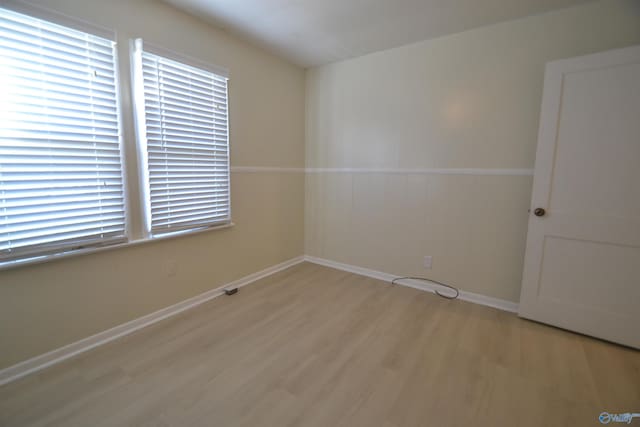 unfurnished room with light wood-style flooring, baseboards, and a wainscoted wall