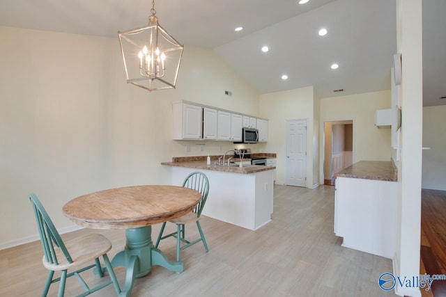 kitchen featuring light wood finished floors, white cabinets, a peninsula, hanging light fixtures, and stainless steel appliances