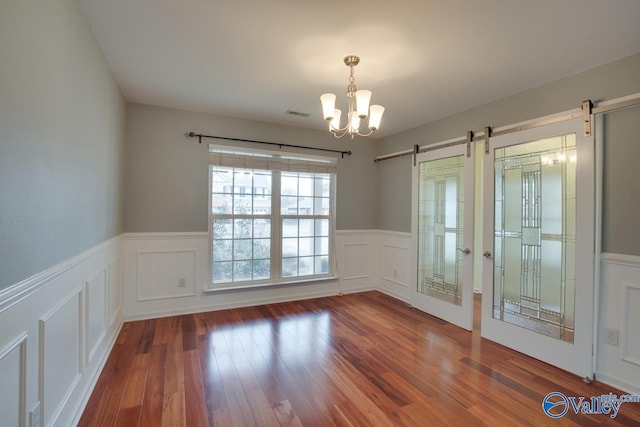 unfurnished room featuring wood finished floors, wainscoting, an inviting chandelier, and a barn door