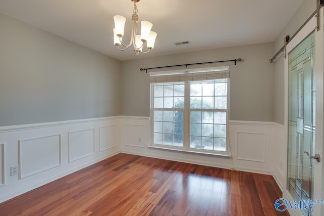 unfurnished room with a barn door, visible vents, a wainscoted wall, wood finished floors, and a notable chandelier