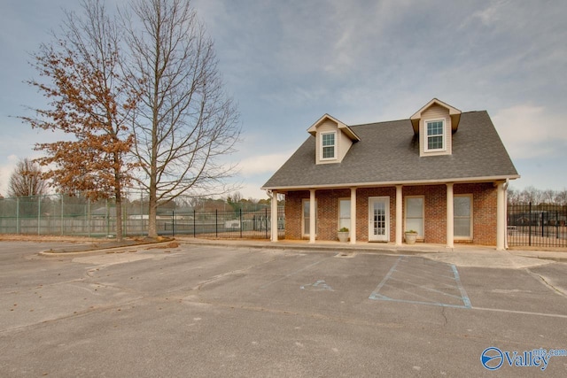 view of front facade with uncovered parking, brick siding, fence, and a shingled roof