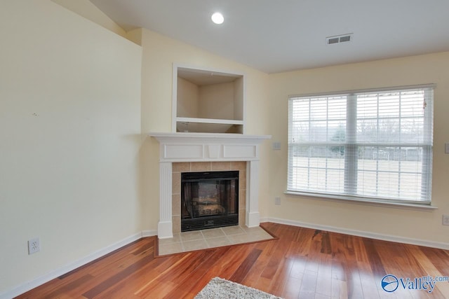 unfurnished living room featuring lofted ceiling, visible vents, wood finished floors, a tile fireplace, and baseboards