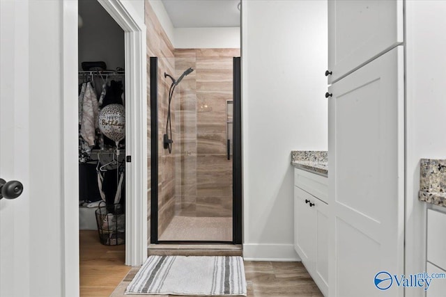 bathroom with vanity, a walk in closet, baseboards, a stall shower, and wood finished floors
