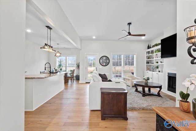living room featuring light wood-style flooring, recessed lighting, a glass covered fireplace, and ceiling fan