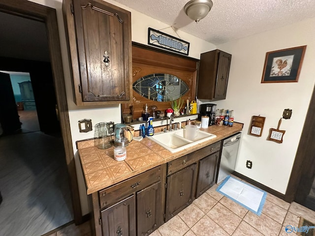 kitchen featuring a textured ceiling, dark brown cabinetry, sink, dishwasher, and light tile patterned flooring