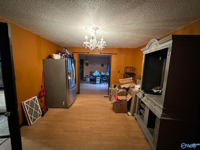 kitchen featuring stainless steel fridge, light wood-type flooring, a textured ceiling, and a notable chandelier