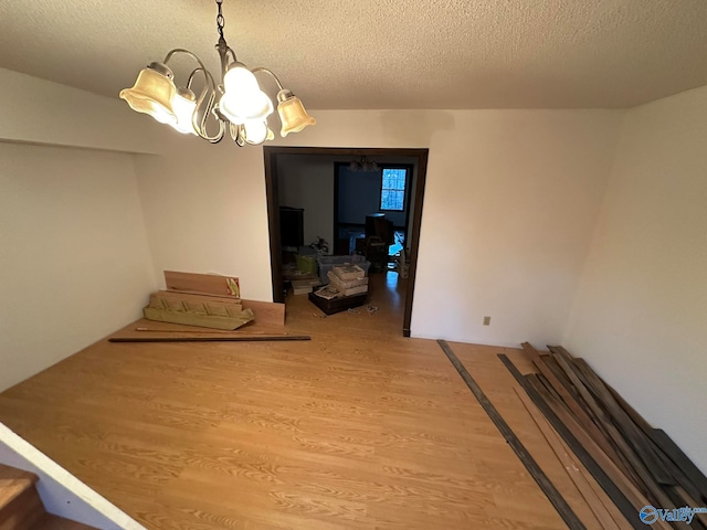 unfurnished dining area featuring hardwood / wood-style flooring, a notable chandelier, and a textured ceiling