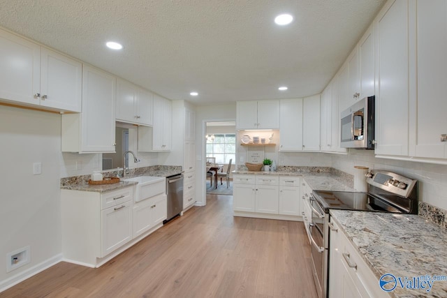 kitchen with light stone counters, stainless steel appliances, light wood-style floors, white cabinetry, and a sink