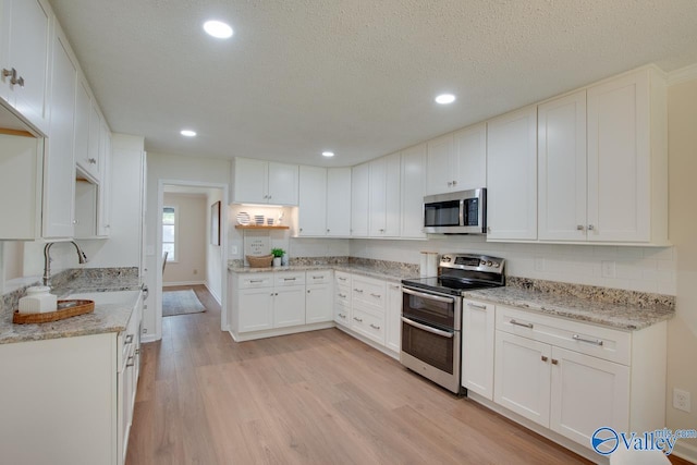 kitchen featuring appliances with stainless steel finishes, light wood-type flooring, white cabinets, and light stone counters