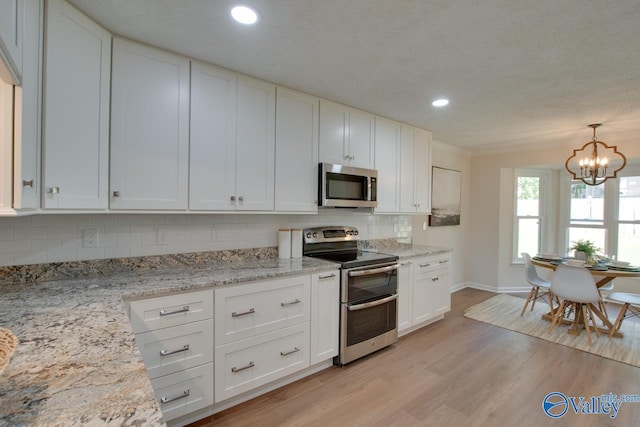 kitchen featuring light wood finished floors, white cabinets, appliances with stainless steel finishes, light stone countertops, and pendant lighting