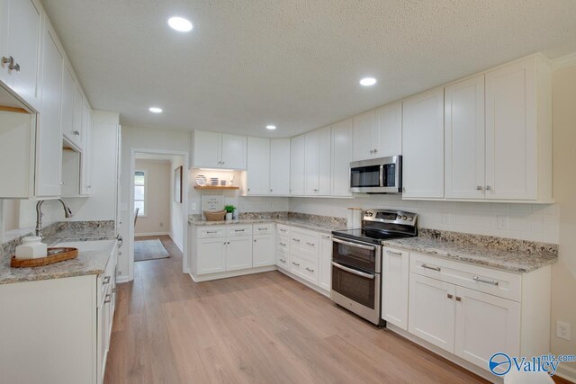 15011 Glory Dr SE, Huntsville, AL 35803 - kitchen with white cabinetry, light stone counters, light wood-style floors, and appliances with stainless steel finishes