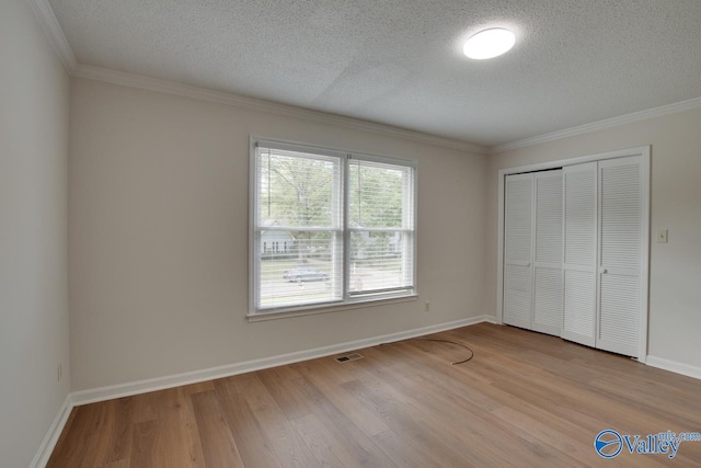 unfurnished bedroom with a textured ceiling, light wood-style flooring, baseboards, a closet, and crown molding