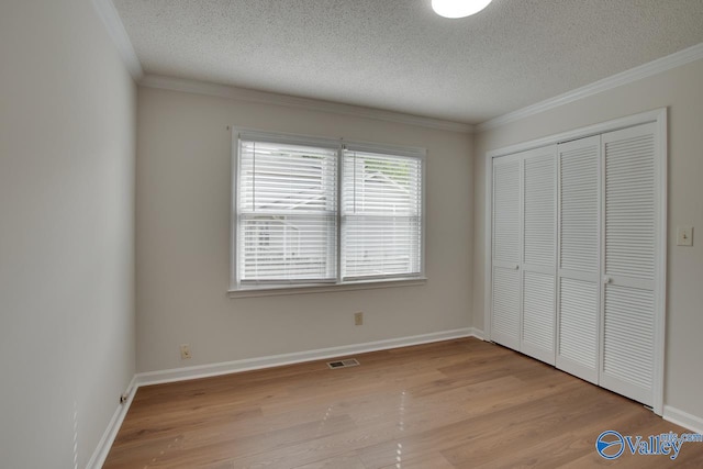 unfurnished bedroom featuring light wood-style floors, visible vents, a textured ceiling, and ornamental molding