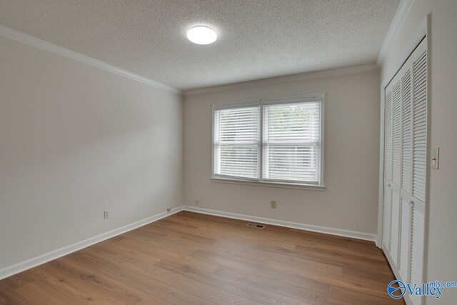 unfurnished bedroom featuring crown molding, light wood finished floors, a closet, a textured ceiling, and baseboards