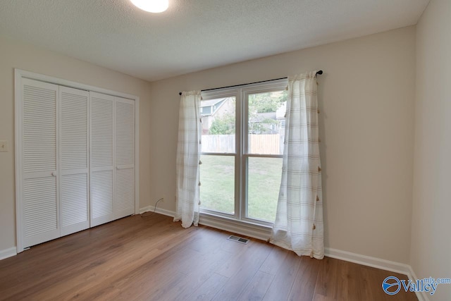 unfurnished bedroom with visible vents, a textured ceiling, baseboards, and wood finished floors