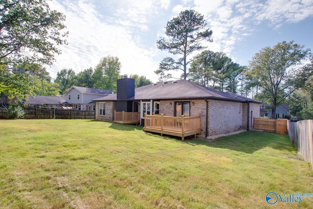 rear view of property featuring a fenced backyard, a chimney, a lawn, and a wooden deck