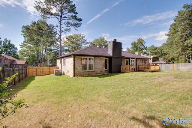 rear view of property featuring a yard, brick siding, a chimney, and a fenced backyard