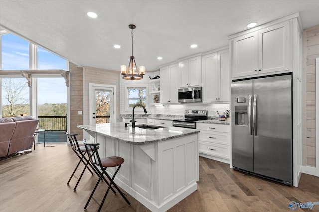 kitchen with stainless steel appliances, sink, white cabinets, an island with sink, and pendant lighting