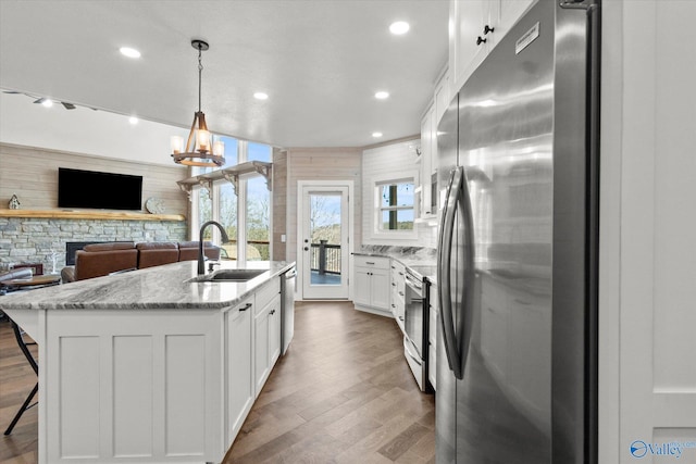 kitchen featuring hanging light fixtures, a kitchen island with sink, white cabinetry, appliances with stainless steel finishes, and sink