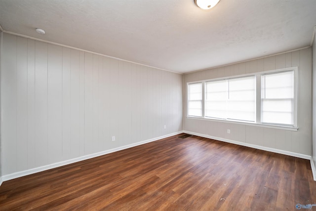 spare room with dark wood-style floors, visible vents, and baseboards